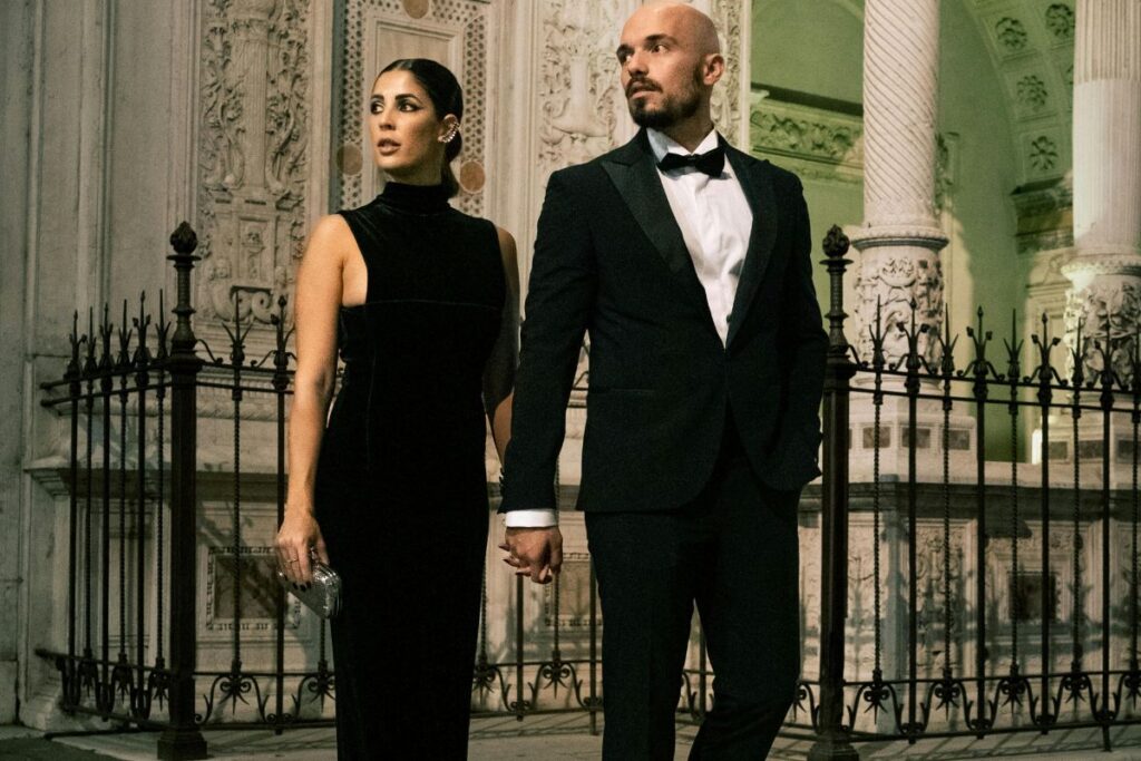 A man in a tuxedo and a woman in an elegant black dress posing in Dillards outfits.